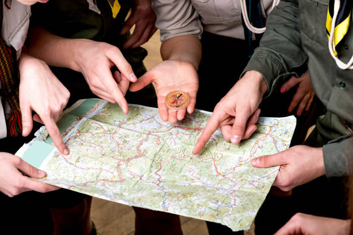 Four young scout members in uniform looking to the map and compass. Close plan without face